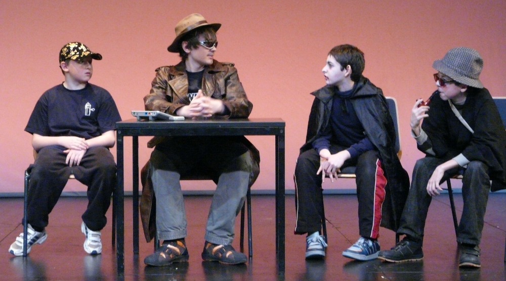 Vier Kinder sitzen auf einer Bühne in Kostümen und spielen ein Theaterstück